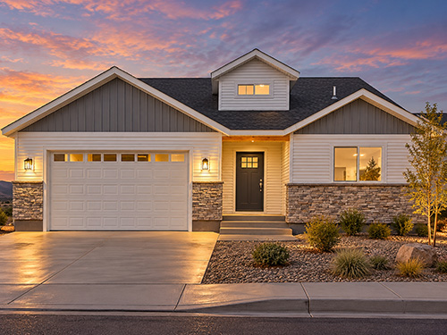 Wright floor plan by Smart Dwellings featuring a two-car garage, stone accents, and welcoming exterior lighting at dusk in Wyoming.>